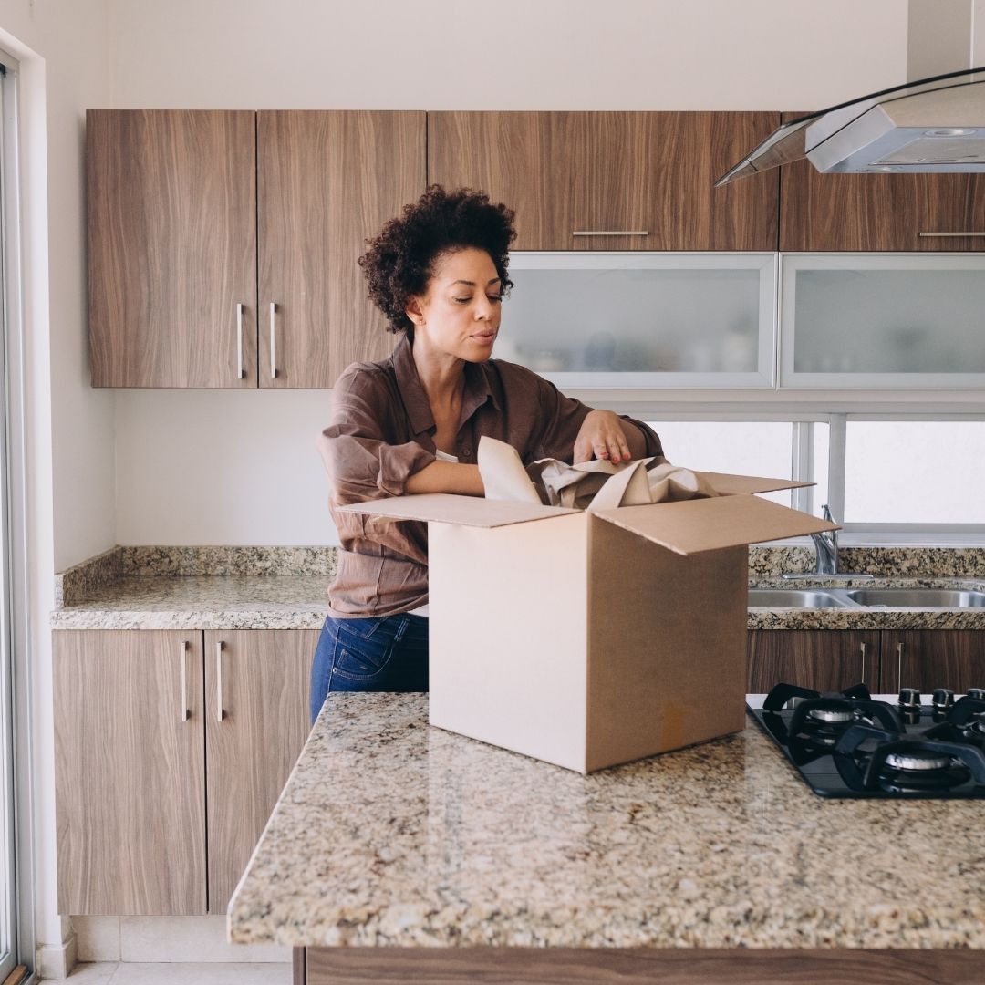 woman packs moving box sitting on kitchen counter