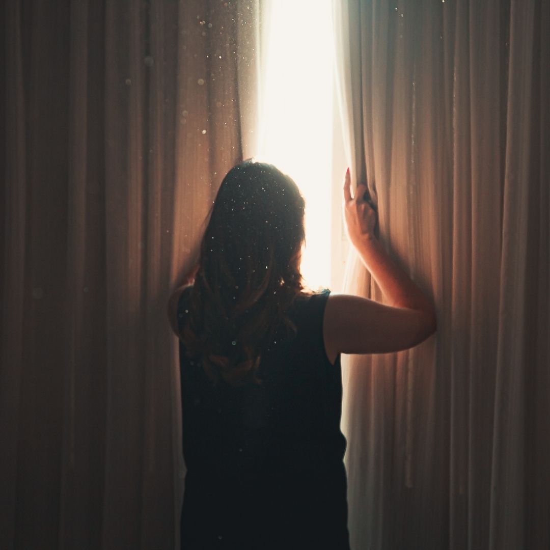 woman open window curtains to let light in