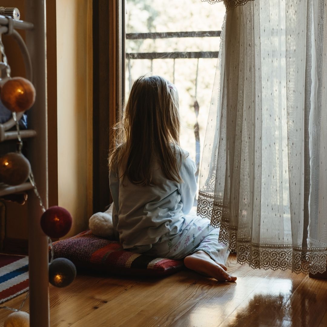 girl sits at window of home