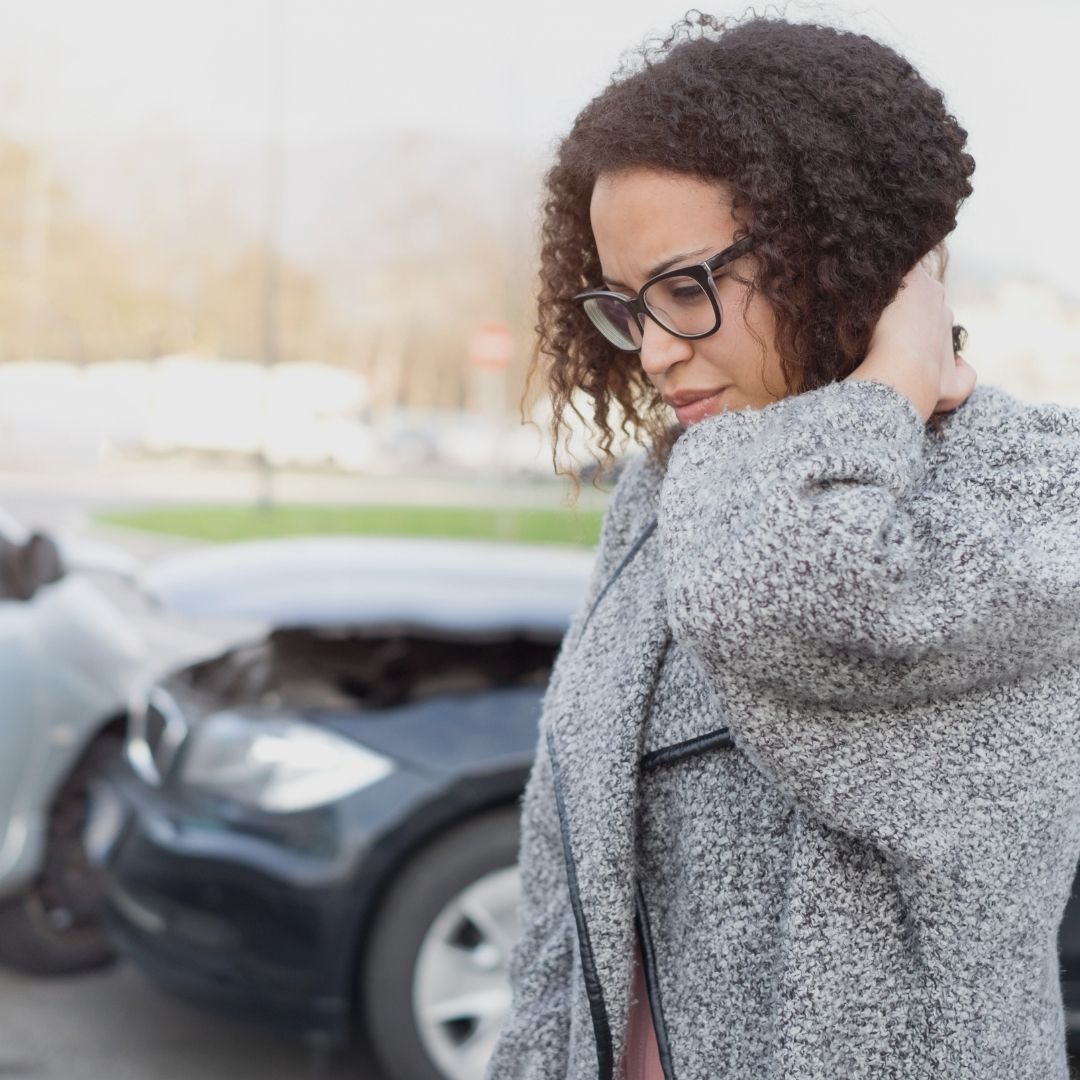 driver near car after accident, holding neck in pain